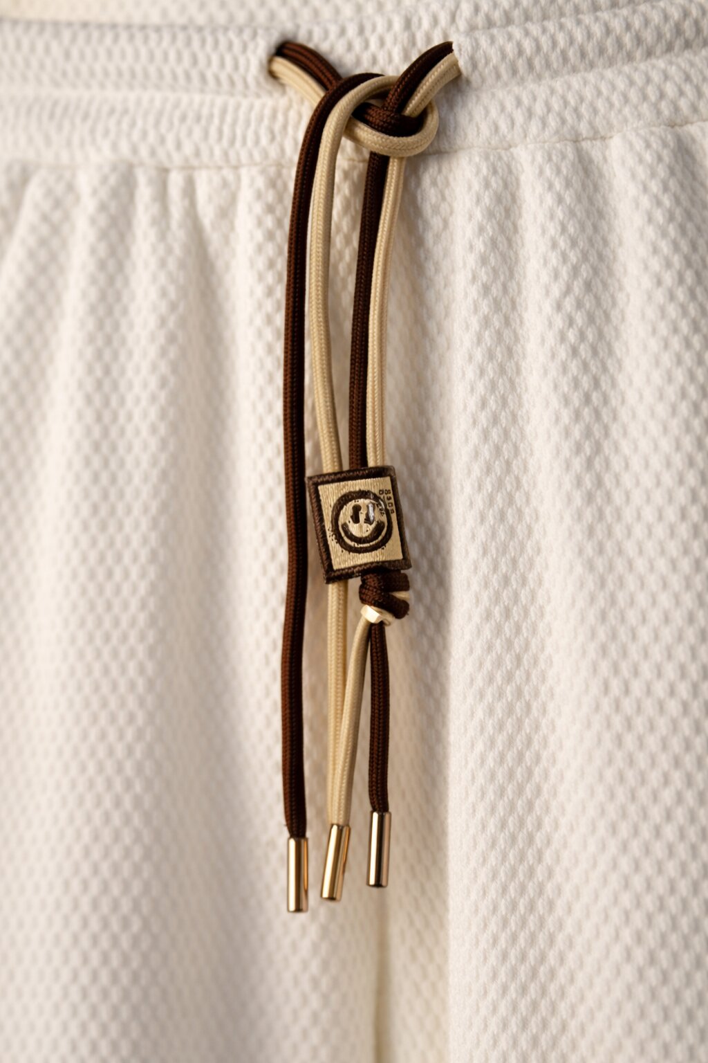 White textured pants close-up with elastic waistband and dual-tone drawstring detail
